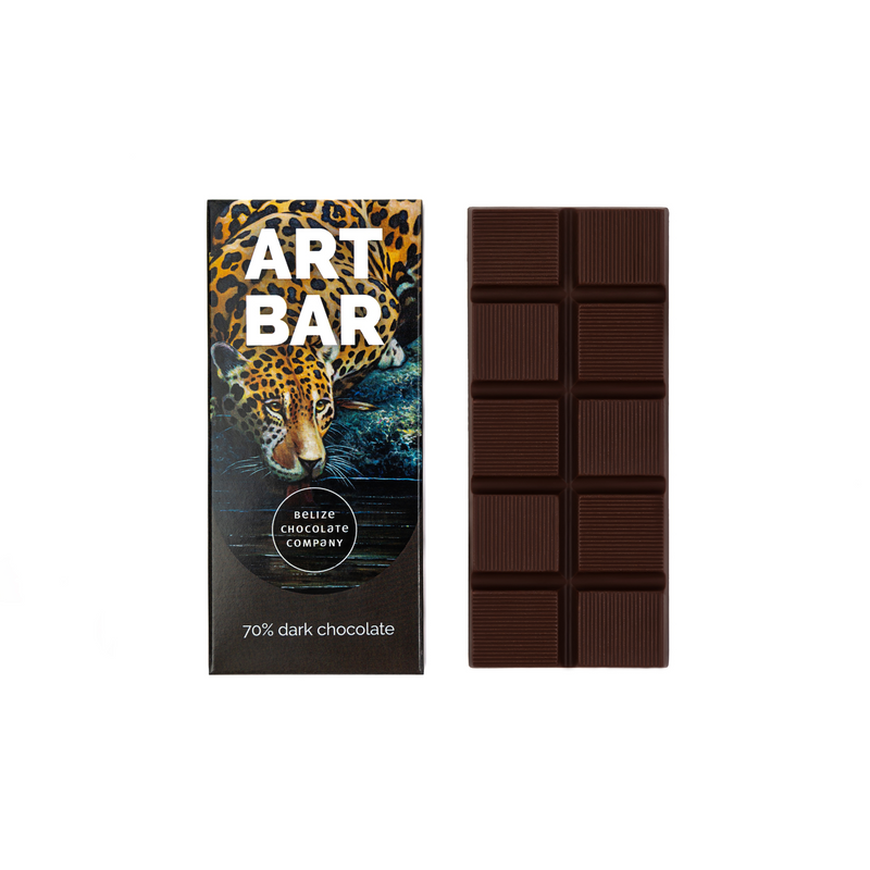 A visually appealing packaging featuring Belizean artwork, including a majestic Jaguar painting by Papo, the national animal of Belize. This packaging promotes creativity, empathy, and support for Belizean school children. It describes the process of making a 70% dark chocolate bar from organic Belizean cacao beans and Orange Walk cane sugar, with tasting notes of raisins, caramel, and cherry. The alt text also mentions international shipping options available from October to April."