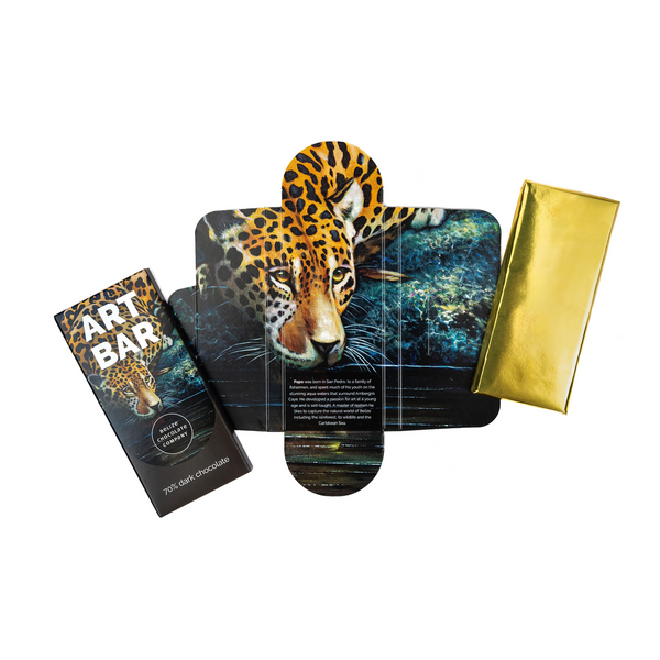 A visually appealing packaging featuring Belizean artwork, including a majestic Jaguar painting by Papo, the national animal of Belize. This packaging promotes creativity, empathy, and support for Belizean school children. It describes the process of making a 70% dark chocolate bar from organic Belizean cacao beans and Orange Walk cane sugar, with tasting notes of raisins, caramel, and cherry. The alt text also mentions international shipping options available from October to April."